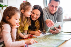 Community Resources for Caregivers. About this photo: Two adults and two children leaning on a table with a map, notebook and tablet